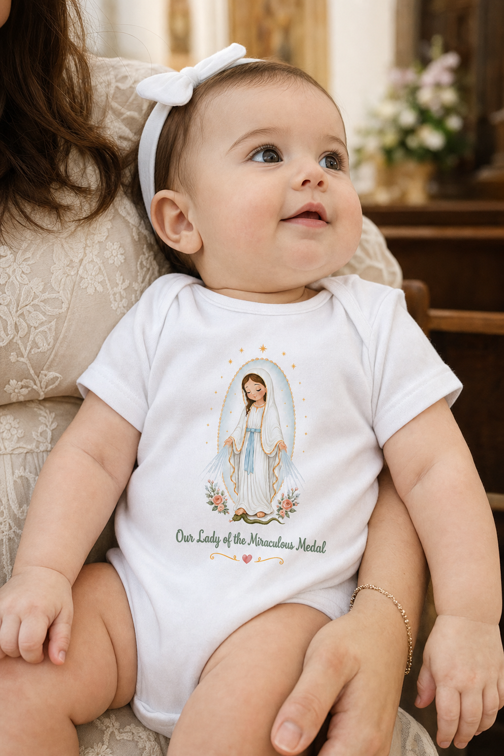 Baby girl wearing the Our Lady of the Miraculous Medal bodysuit in a lifestyle setting — detail