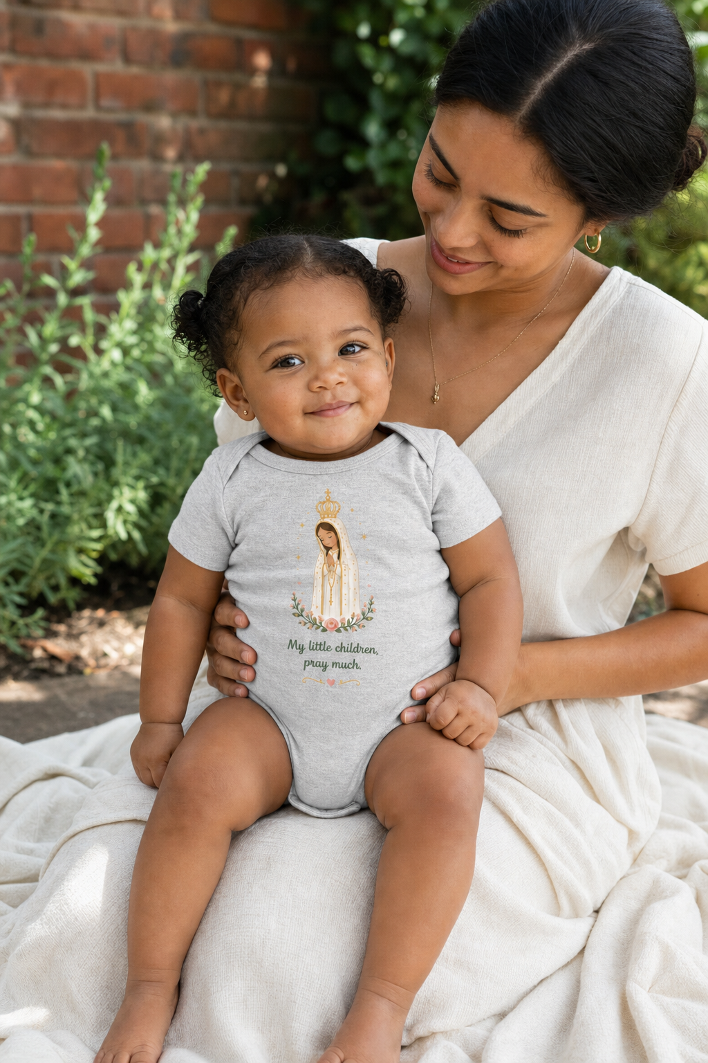 Baby girl wearing the Pray Much Fátima Baby Bodysuit in Athletic Heather