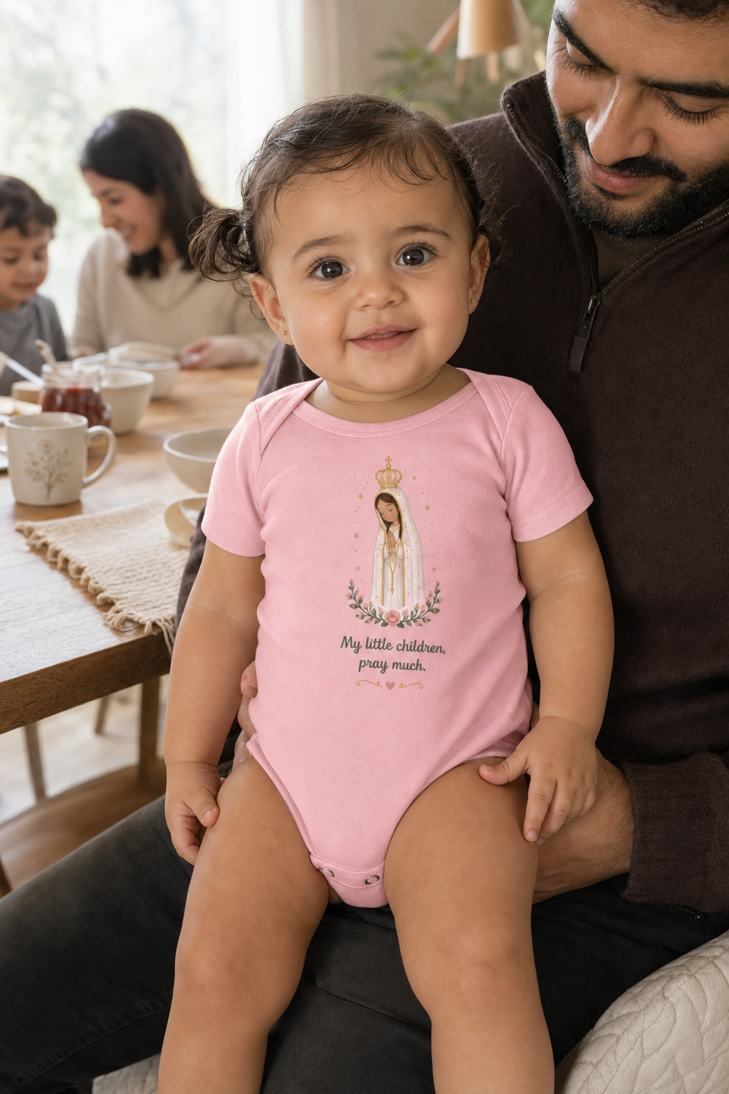 Baby girl wearing the Pray Much Fátima Baby Bodysuit in Pink