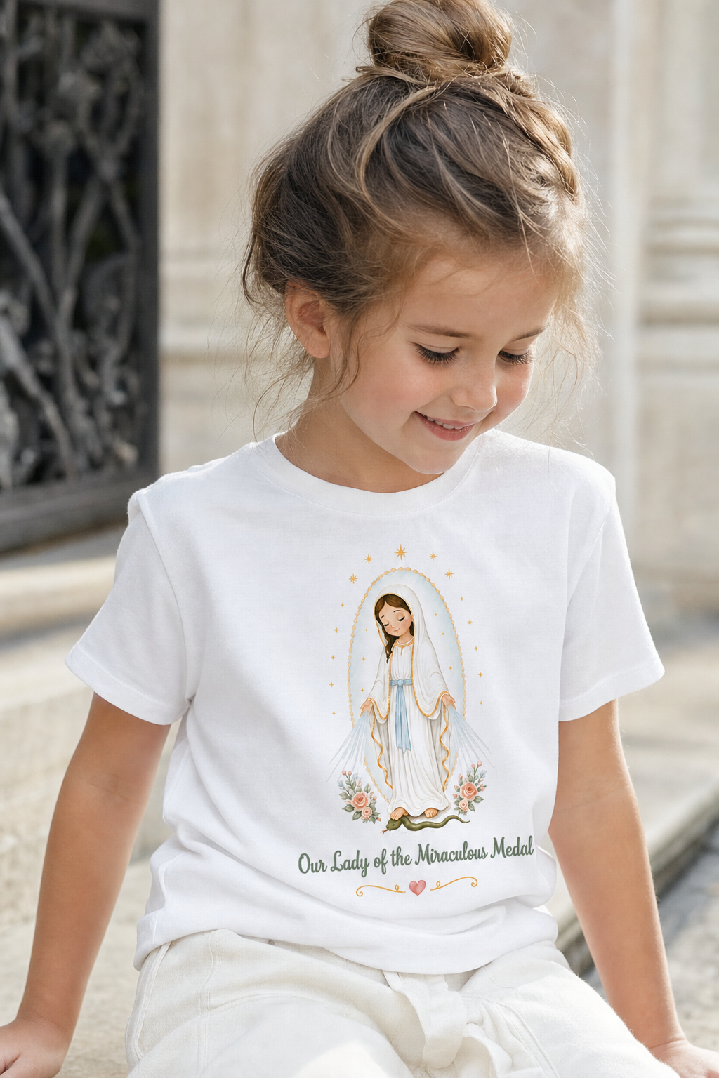 Little girl wearing the Our Lady of the Miraculous Medal toddler T-shirt in a lifestyle setting — detail